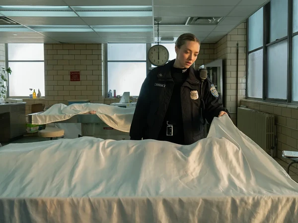 A policewoman in Long Bright River examines a body covered by a sheet.