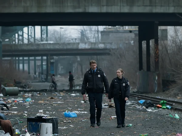 Two police officers walk through a litter - filled area in Long Bright River.