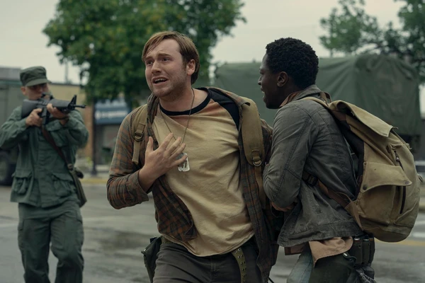 Two men face a soldier with a gun in The Long Walk.