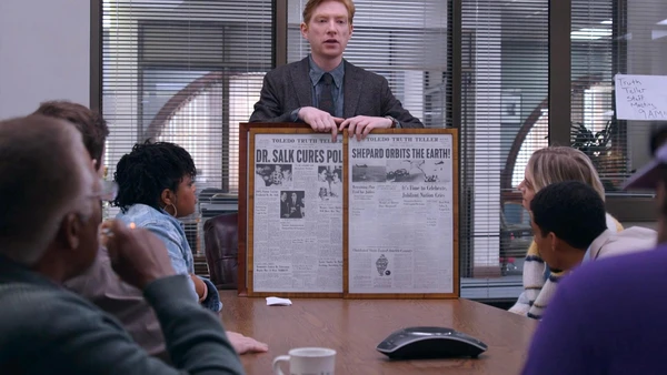 The publisher in The Paper presents something to a group in a meeting room.