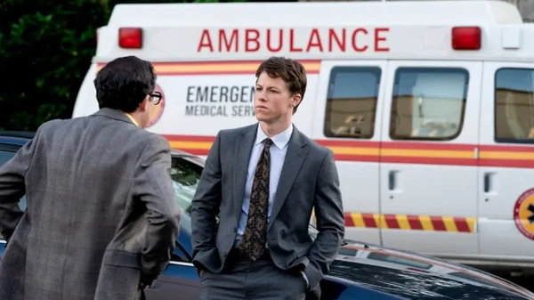 A lawyer engages in conversation outside, with an ambulance in the background in The Rainmaker.
