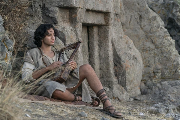 A man plays a harp by a rocky structure in House of David.